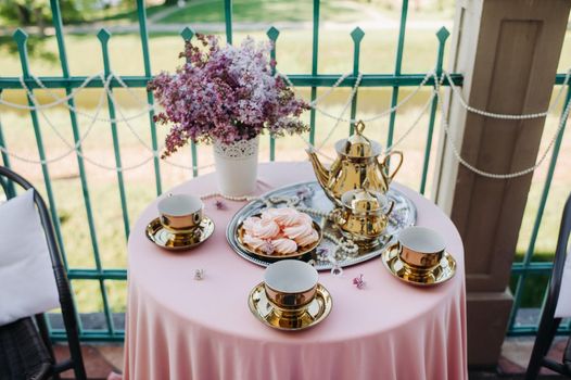 Delicate morning tea table setting with lilac flowers, antique spoons and dishes on a table with a pink tablecloth.