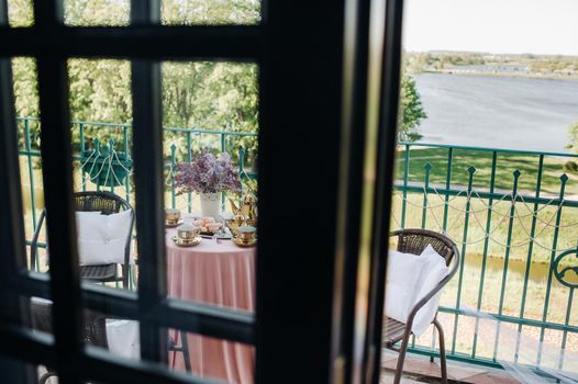 Delicate morning tea table setting with lilac flowers in Nesvizh castle, antique spoons and dishes on the table with a pink tablecloth.