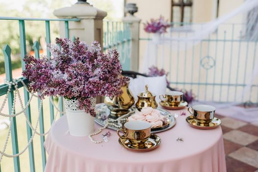 Delicate morning tea table setting with lilac flowers, antique spoons and dishes on a table with a pink tablecloth.