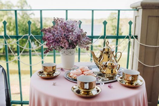 Delicate morning tea table setting with lilac flowers, antique spoons and dishes on a table with a pink tablecloth.