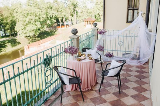 Delicate morning tea table setting with lilac flowers in Nesvizh castle, antique spoons and dishes on the table with a pink tablecloth.