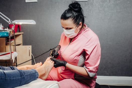 The master makes a pedicure in the beauty salon. The girl in a blue mask and gloves makes cosmetic procedures. Blonde and brunette in a beauty salon. Pure flowers in a tub with water.