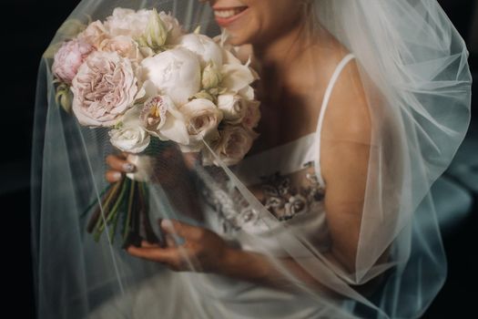 wedding bouquet with peonies in the hands of the bride under the veil.Morning of the bride.