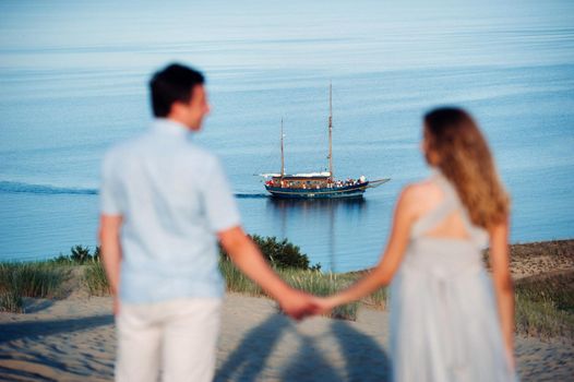 A couple in love stands on the beach in the dunes against the background of the Baltic sea and a ship, a Couple on the beach close-up in Lithuania, Nida.