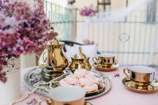 Delicate morning tea table setting with lilac flowers, antique spoons and dishes on a table with a pink tablecloth.