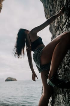 A girl climbs a rock. The athlete trains in nature. Woman overcomes difficult climbing route. Extreme hobby. Tourist woman rock climber hiking on mountains rocks over beautiful sea coast
