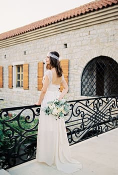 Bride with a bouquet stands on a bridge near an old stone building. High quality photo