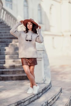 Woman walks in the city, lifestyle. Young beautiful woman in a loose light sweater, brown skirt and sneakers with a hat