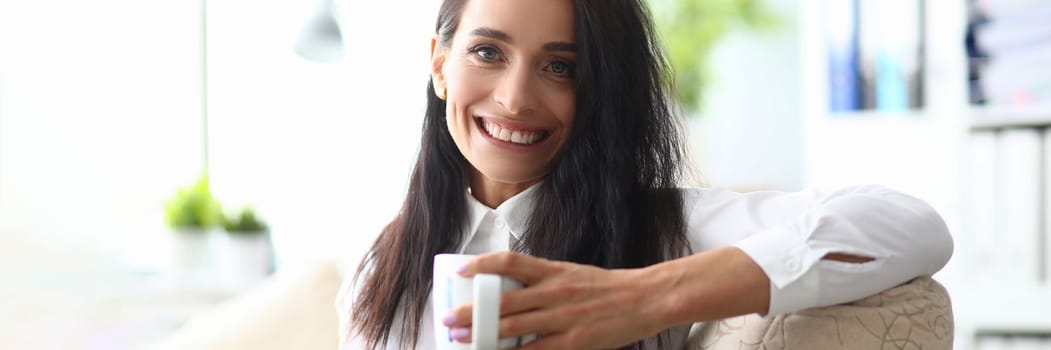 Portrait of smiling minded successful employee business woman in white shirt with cup. Concept of career achievement and rest in workplace