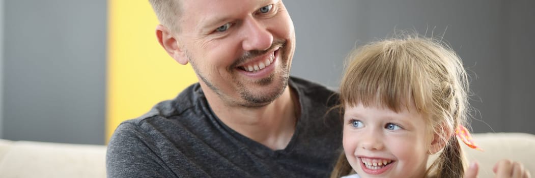 Happy dad holding cute cheerful daughter laughing and having good time together. Loving father and smiling little girl hugging and caring dad