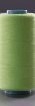 Light green spool of thread on gray background. Sewing machine materials and high-quality durable threads