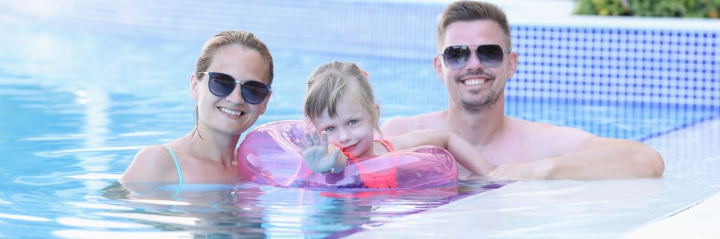 Portrait of young family with smiling child in pool. Happy joyful family together in pool