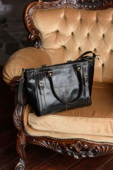 close-up photo of blackleather bag on a yellow velor vintage armchair. indoor photo