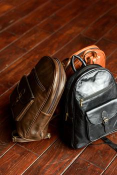 three different colored leather backpacks on a wooden floor. Indoor photo