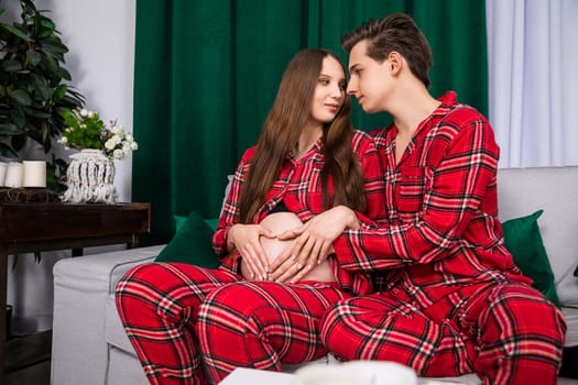 A boy and a girl sit on a light gray sofa and look deeply into each other's eyes. The setting is romantic and there are a lot of accessories in dark green, such as, pillows.