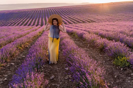 Woman lavender field sunset. Romantic woman walks through the lavender fields. illuminated by sunset sunlight. Dressed in a dress with a hat