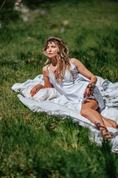 woman sleeps on a white bed in the fresh spring grass in the garden. Dressed in a blue nightgown