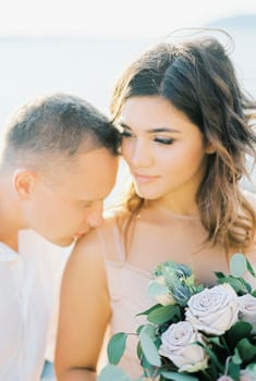 Groom kisses bride with a bouquet on her shoulder. Portrait. High quality photo