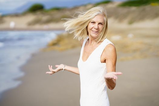 Smiling mature female opening her arms on a tropical beach. Elderly woman enjoying her retirement walking on the beach.