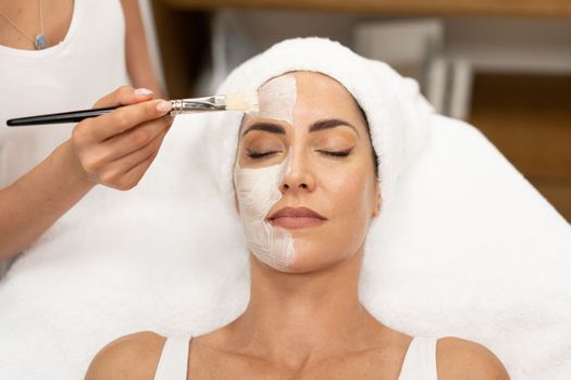 Aesthetics applying a mask to the face of a Middle-aged woman in modern wellness center. Beauty and Aesthetic concepts.