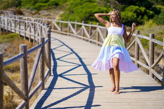 Young African woman wearing a beautiful dress on a boardwalk on the beach.