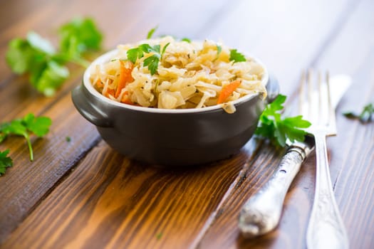 Braised cabbage with carrots, onions and herbs in a ceramic bowl on a wooden table.