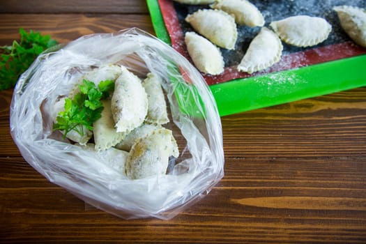 Raw green dough dumplings with parsley, dill. Raw dumplings in a bag on a wooden table.