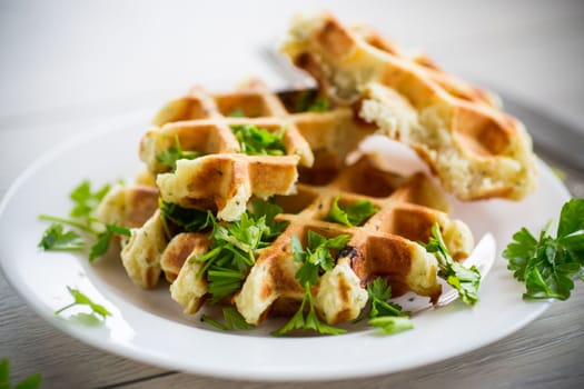 fried Belgian vegetable waffles with spices and herbs, in a plate on a light wooden table.