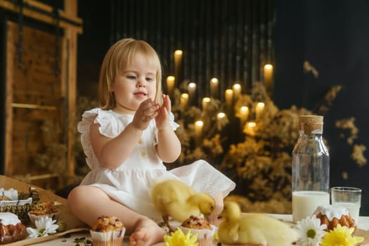 A little girl is sitting on the Easter table and playing with cute fluffy ducklings. The concept of celebrating happy Easter