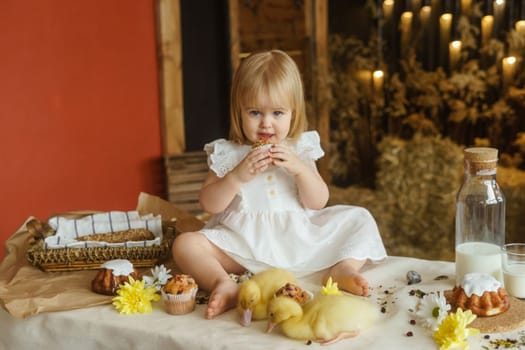A little girl is sitting on the Easter table and playing with cute fluffy ducklings. The concept of celebrating happy Easter
