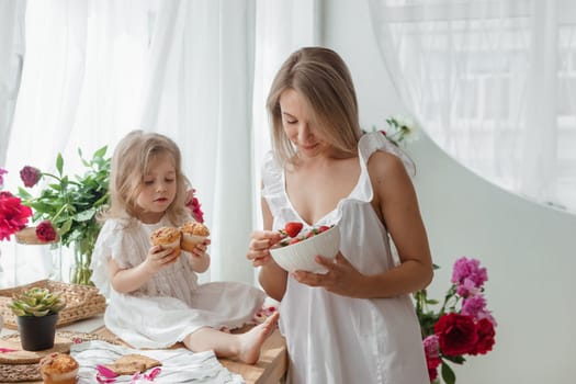 A little blonde girl with her mom on a kitchen countertop decorated with peonies. The concept of the relationship between mother and daughter. Spring atmosphere.