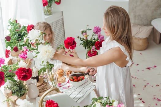 A little blonde girl with her mom on a kitchen countertop decorated with peonies. The concept of the relationship between mother and daughter. Spring atmosphere.