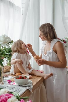 A little blonde girl with her mom on a kitchen countertop decorated with peonies. The concept of the relationship between mother and daughter. Spring atmosphere.