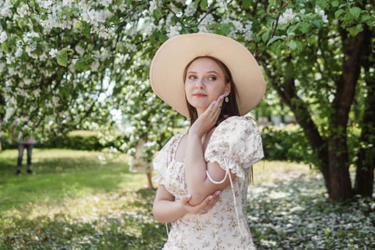 An attractive long-haired woman walks in the spring in the park of blooming apple trees. Spring portrait of a woman