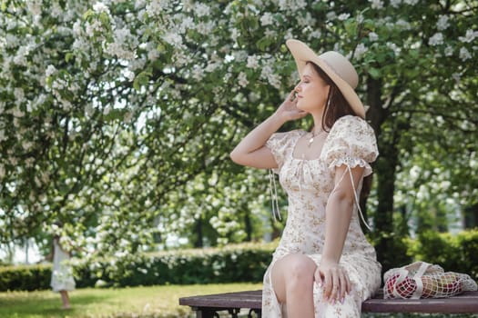 An attractive long-haired woman walks in the spring in the park of blooming apple trees. Spring portrait of a woman