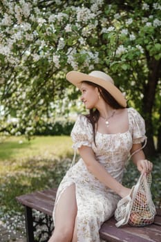 An attractive long-haired woman walks in the spring in the park of blooming apple trees. Spring portrait of a woman