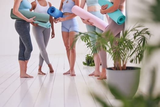 Feet of women standing in a yoga studio cropped. Group of friends ready for yoga practice. Women holding yoga equipment in the studio. Women waiting for pilates practice to begin