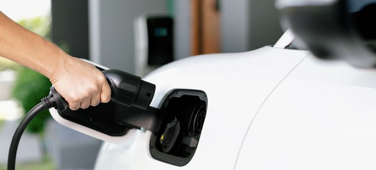 Progressive concept of hand insert an emission-free power connector to the battery of electric vehicle at home. Electric vehicle charging via cable from charging station to EV car battery