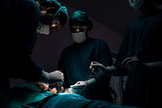 Surgical team performing surgery to patient in sterile operating room. In a surgery room lit by a lamp, a professional and confident surgical team provides medical care to an unconscious patient.