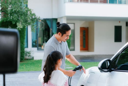 Progressive father and daughter returned from school in electric vehicle that is being charged at home. Electric vehicle driven by renewable clean energy. Home charging station concept for environment