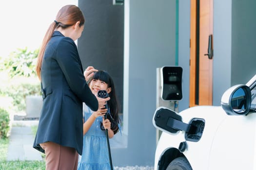 Progressive lifestyle of mother and daughter who have just returned from school in an electric vehicle that is being charged at home. Electric vehicle powered by sustainable clean energy.