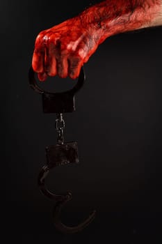 Faceless man holding handcuffs black background. Hands are stained with blood