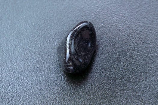 Close up of natural mineral from geological collection tumbled black onyx gem stone, black background