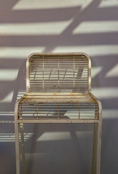 The white metal chair is stand alone in front of the white wall with sunlight shine through. Space for text, Selective focus.