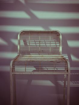The metal chair is stand alone in front of the white wall with Sunbeam shine through in the morning. Retro style, Copy space, Selective focus.