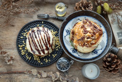 Two Homemade Soft Chocolate Buns, Caramel Pecanbon topped with caramel frosting and pecans and Cinnamon roll topped with rich cream cheese frosting served with Metal fork on old rustic wooden table. The concept of delicious dessert, Top view, Selective focus.