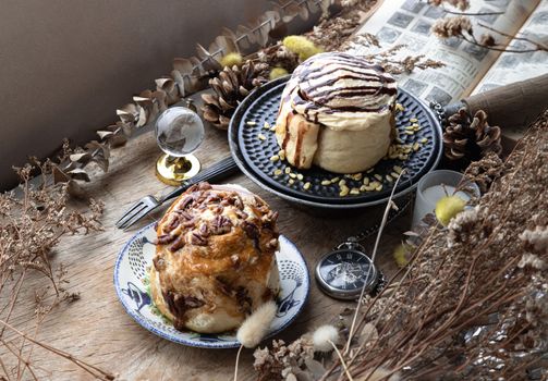 Two Homemade Soft Chocolate Buns, Caramel Pecanbon topped with caramel frosting and pecans and Cinnamon roll topped with rich cream cheese frosting served with Metal fork on old rustic wooden table. The concept of delicious dessert, Top view, Selective focus.