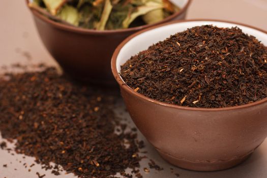 A large and chalky leaf of black tea in two porcelain brown cups. Green tea in clay teacup. Tea leaf for brewing.