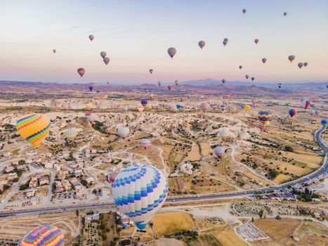 Colorful hot air balloons flying over at fairy chimneys valley in Nevsehir, Goreme, Cappadocia Turkey. Spectacular panoramic drone view of the underground city and ballooning tourism. High quality.