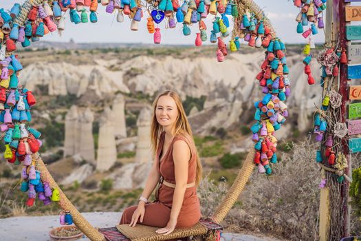 Young woman exploring valley with rock formations and fairy caves near Goreme in Cappadocia Turkey. Wish tree. Small multi-colored jugs with inscriptions, wishes hanging on the branches of a tree., against the backdrop of sand ruins and blue sky.